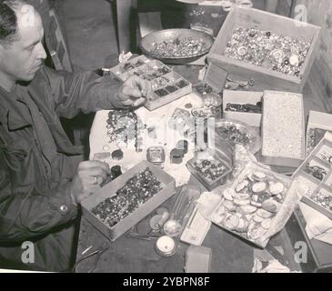 Un soldato americano vede una serie di pietre e altri oggetti di valore confiscati ai prigionieri nel campo di concentramento di Buchenwald e recuperati dalle truppe statunitensi dopo la liberazione della camma Foto Stock