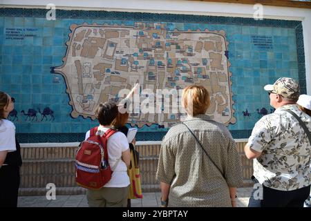 Khiva, Uzbekistan - 15 settembre 2024: Un gruppo di turisti ascolta una guida turistica vicino alla mappa del centro storico di Khiva sulle piastrelle di ceramica Foto Stock