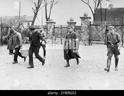 Le guardie dell'SA sorvegliano i prigionieri che stanno trasportando una vasca vicino all'ingresso del campo di concentramento di Oranienburg. La foto è datata 1933, quindi questi uomini sono stati imprigionati entro mesi dalla presa del potere da parte di Hitler. In quanto tali sono probboricamente membri del partito comunista. Foto Stock