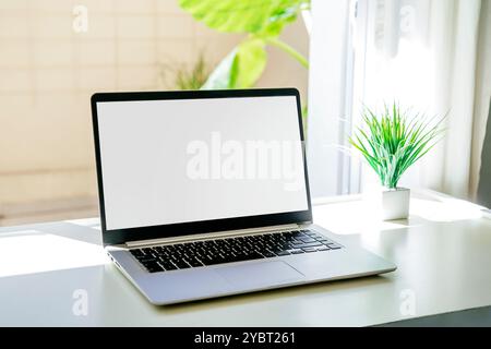 Computer portatile su una scrivania con schermo bianco per il mockup. Non ci sono persone sulla scena. Computer accanto alla finestra. Scattare fotografie con colori chiari e luminosi Foto Stock