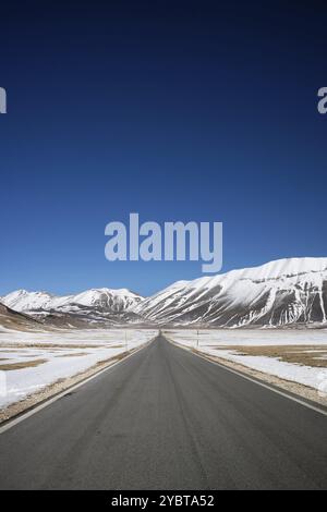 Vista della lunga e dritta strada panoramica che porta a Castelluccio di Norcia nel centro Italia Foto Stock