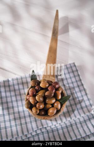 Presentazione di un piccolo gruppo di olive nere su mestolo di legno Foto Stock