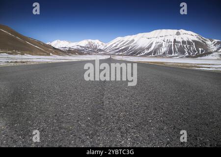 Vista della lunga e dritta strada panoramica che porta a Castelluccio di Norcia nel centro Italia Foto Stock