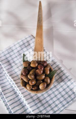 Presentazione di un piccolo gruppo di olive nere su mestolo di legno Foto Stock