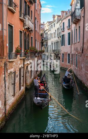 Dall'alto di anonimi gondolieri maschi che guardano in basso mentre remi in piedi su lunghe barche strette nell'acqua del canale di Venezia tra gli edifici in pieno giorno Foto Stock