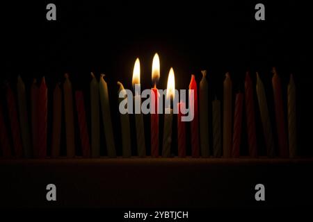 Serie di piccole candele accese su sfondo nero Foto Stock