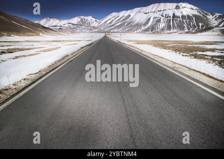 Vista della lunga e dritta strada panoramica che porta a Castelluccio di Norcia nel centro Italia Foto Stock