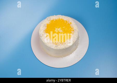 Piccola torta di cocco decorata con una fetta di arancia e perle bianche su sfondo blu Foto Stock