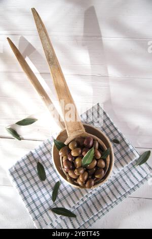 Presentazione di un piccolo gruppo di olive nere su mestolo di legno Foto Stock