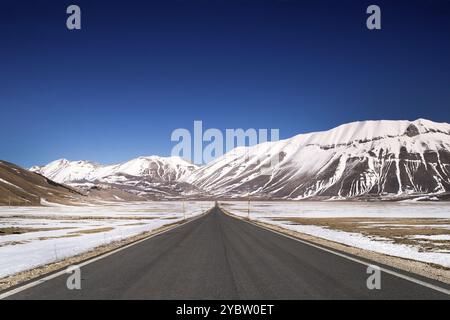 Vista della lunga e dritta strada panoramica che porta a Castelluccio di Norcia nel centro Italia Foto Stock