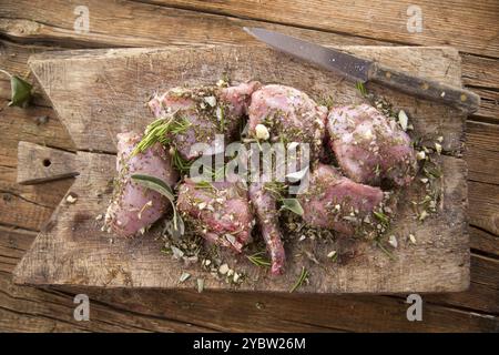 Preparazione con erbe aromatiche mediterranee tritate di porzioni di coniglio crudo Foto Stock