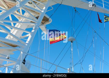 Barcellona. Espain -20 ottobre 2024: Immagine di un albero di nave con bandiere spagnole e dell'Unione europea, catturato in movimento sotto un cielo blu. Perfetto per i rappresentanti Foto Stock