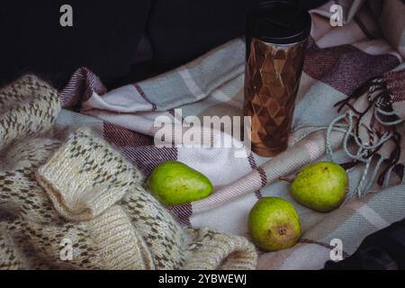 Maglione lavorato a maglia, tre frutti di pera e tazza thermos su coperta a scacchi nel bagagliaio aperto dell'auto. Natura morta autunnale. Picnic su strada. Viaggiare stile di vita momen Foto Stock