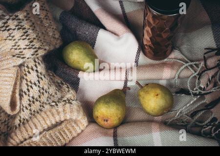 Maglione lavorato a maglia, tre frutti di pera e tazza thermos su coperta a scacchi nel bagagliaio aperto dell'auto. Natura morta autunnale. Picnic su strada. Viaggiare stile di vita momen Foto Stock