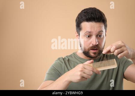 Uomo triste che prende i capelli persi dal pettine su sfondo beige, spazio per il testo. Problema di alopecia Foto Stock