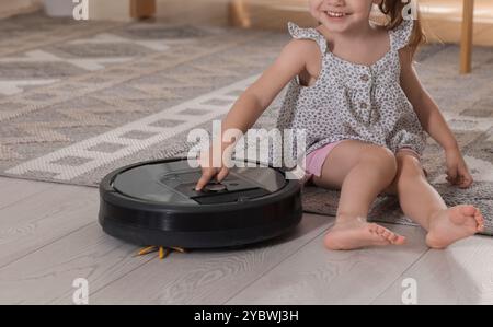 Bambina con aspirapolvere robotizzato sul pavimento di casa, primo piano Foto Stock