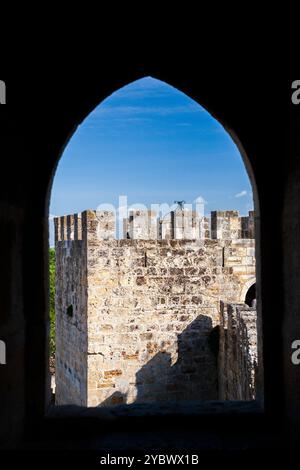 Esplora la splendida architettura del castello di San Giorgio, con i suoi merli iconici incorniciati da una finestra ogivale. Foto Stock