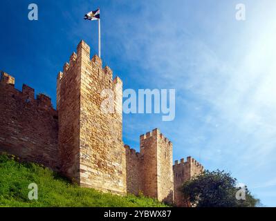 La bandiera di Lisbona fluttua graziosamente in cima allo storico castello di San Giorgio, mostrando le sue maestose pareti di pietra contro un vivace cielo blu in Portogallo. Foto Stock