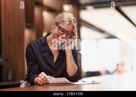 Una donna professionista impegnata in una conversazione telefonica mentre lavora in ufficio Foto Stock