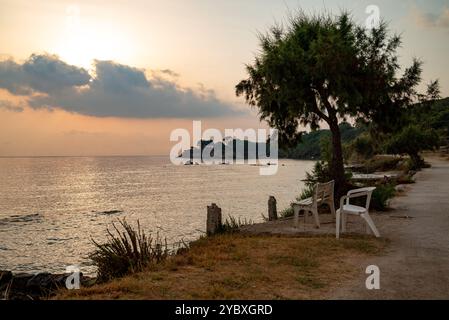Sedie bianche sulla spiaggia di Zante per rilassarsi in tranquillità durante l'ora d'oro. Un posto tranquillo vicino al mare, perfetto per un momento di pace. Foto Stock