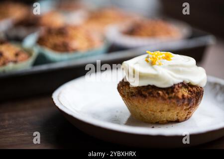 Un cupcake appena sfornato ricoperto di cremosa glassa e una spruzzata di scorza d'arancia, perfetto per un dolce e agrumato appagante. Foto Stock