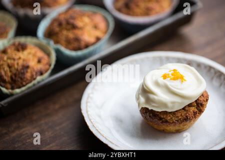 Un cupcake appena sfornato ricoperto di cremosa glassa e una spruzzata di scorza d'arancia, perfetto per un dolce e agrumato appagante. Foto Stock