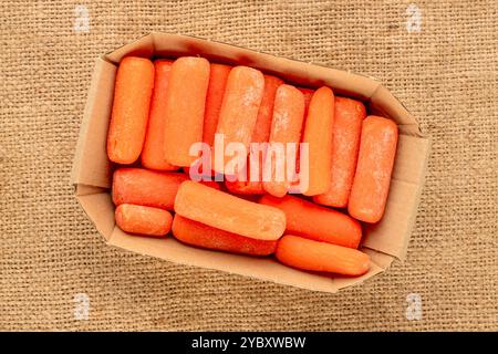 Piccola carota sbucciata con piastra di carta su panno di iuta, macro, vista dall'alto. Foto Stock