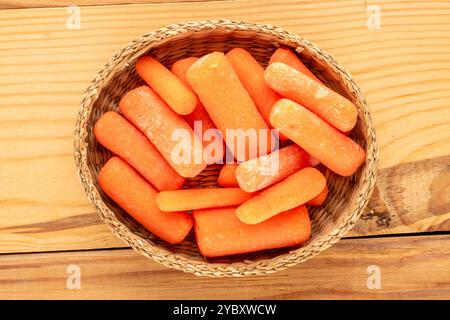 Piccole carote pelate in un piatto di paglia su un tavolo di legno, vista ravvicinata dall'alto. Foto Stock