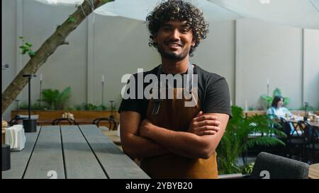 Fiducioso gioioso indiano arabo etnico uomo uomo uomo sorridente lavoratore di caffè in grembiule Guy cameriere barista più pulito proprietario di una piccola impresa che guarda la macchina fotografica Foto Stock