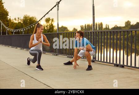 Giovane coppia allegra che fa esercizi sportivi di stretching in natura in piedi sul ponte. Foto Stock