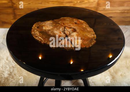 Un elegante tavolo rotondo che mostra uno splendido piano in legno pietrificato, elegantemente esposto su un caldo sfondo in legno, perfetto per interni moderni Foto Stock