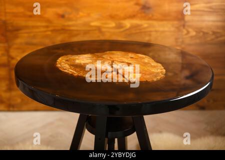 Un elegante tavolo rotondo che mostra uno splendido piano in legno pietrificato, elegantemente esposto su un caldo sfondo in legno, perfetto per interni moderni Foto Stock