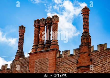 I camini in mattoni Tudor si innalzano contro un vibrante cielo blu con soffici nuvole bianche all'Hampton Court Palace Foto Stock