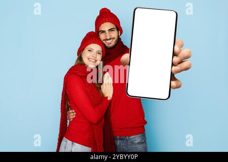 Giovane coppia in maglioni rossi sorridente e con un telefono sullo sfondo blu Foto Stock