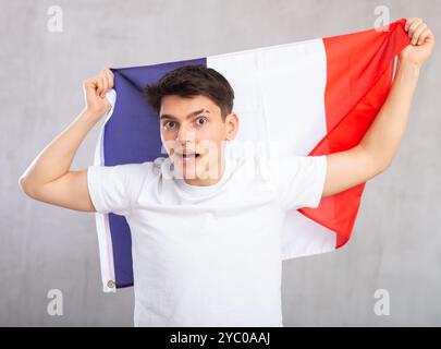 Eccitato, attivo spettatore maschile detiene bandiera nazionale della Francia in mani e canti slogan popolare Foto Stock