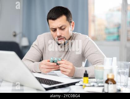 Giovane uomo in cerca di informazioni sui medicinali sul portatile Foto Stock