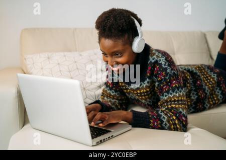 Una giovane donna ama la musica e lavora su un notebook nella sua accogliente casa, adottando la tecnologia moderna Foto Stock