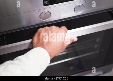 Una persona sta usando la mano per aprire un forno moderno, impegnandosi in attività culinarie a casa Foto Stock