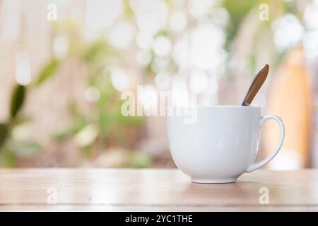 Una tazza di caffè mattutina su un tavolo di legno con bokeh sfocato dagli alberi sullo sfondo. Foto Stock