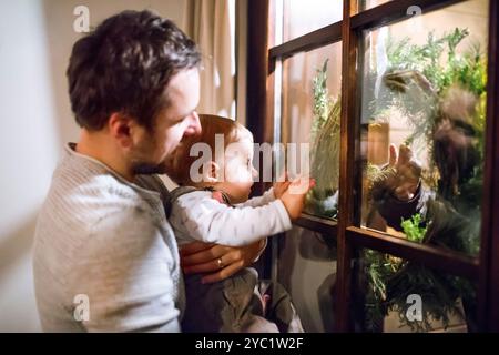 Bambino piccolo con padre che guarda fuori dalla finestra ghiacciata. Magia e atmosfera natalizia per i bambini piccoli. Foto Stock