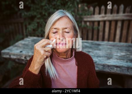 Le donne anziane si sentono malate, usando spray nasale per aiutare a congestione, peluria. Foto Stock