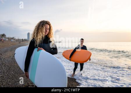 Due giovani surfisti felici con tavola da surf si preparano a colpire le onde al tramonto. Vacanza sportiva attiva Foto Stock