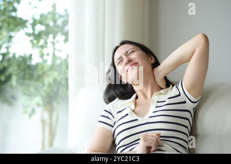 Stressata donna asiatica che soffre mal di collo seduta su un divano scomodo a casa Foto Stock