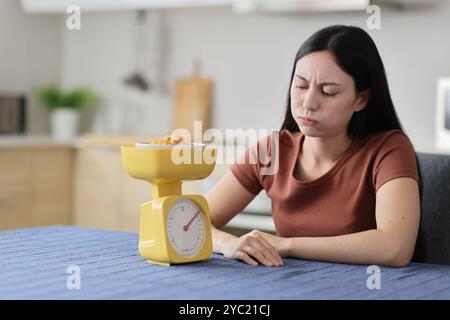 Donna asiatica stressata che pesa il cibo con la bilancia in cucina a casa Foto Stock