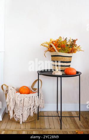 Decorazioni autunnali, tavolo nero con cesto in tessuto pieno di fogliame stagionale e piccola zucca arancione e cestino contenente zucche decorative in ho Foto Stock
