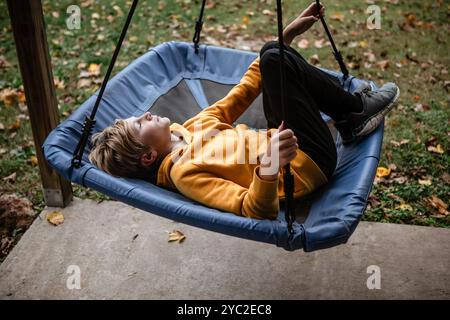 Bambini in felpa gialla che si rilassano su un albero altalena all'aperto in autunno Foto Stock