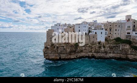 Arroccato su una scogliera rocciosa, il pittoresco villaggio di Puglia vanta edifici imbiancati che si affacciano sullo scintillante mare blu, mentre le spettacolari nuvole si stagliano sopra la testa, Polignano a Mare Italia Foto Stock