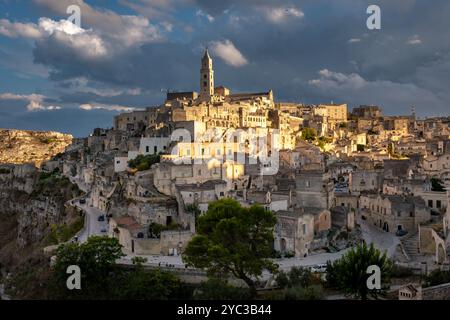 Incastonata in un paesaggio roccioso, Matera Italia rivela le sue splendide abitazioni nelle grotte immerse nella luce soffusa del sole, mentre le spettacolari nuvole si stagliano in alto, in mostra Foto Stock