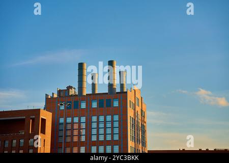 Edificio industriale con alti camini che si innalzano contro il cielo azzurro. Infrastrutture urbane e di produzione durante il tramonto. Moderna centrale elettrica in mattoni b Foto Stock