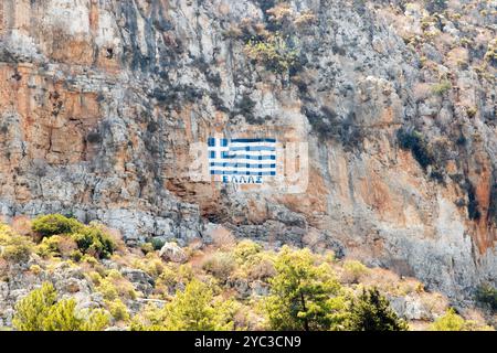 Una bandiera greca dipinta su una scogliera con le parole Grecia scritte in alfabeto greco, sopra l'isola greca di Kastellorizo o Meis in Grecia, Europa Foto Stock